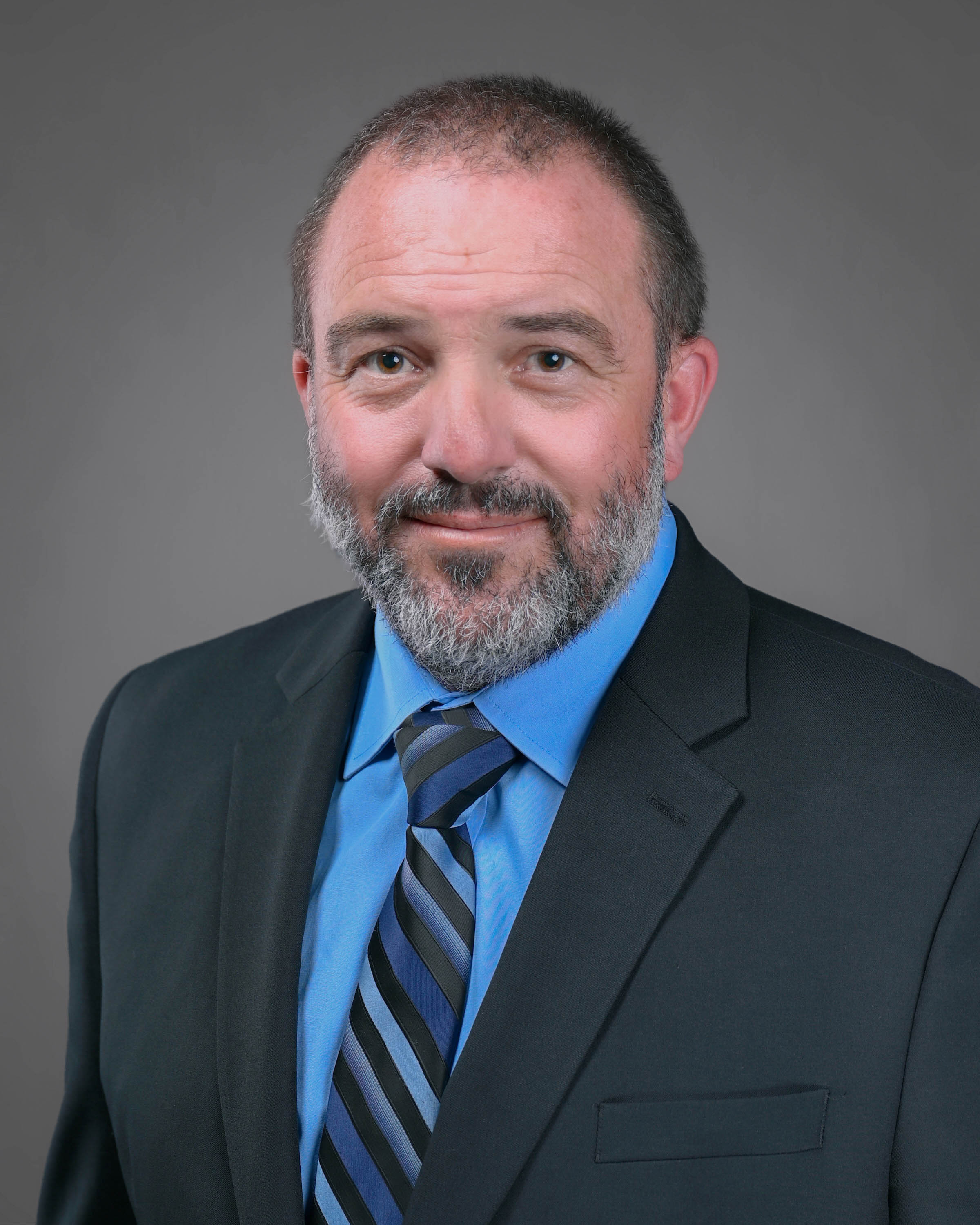 Man with really short hair and a beard wearing a dark suit